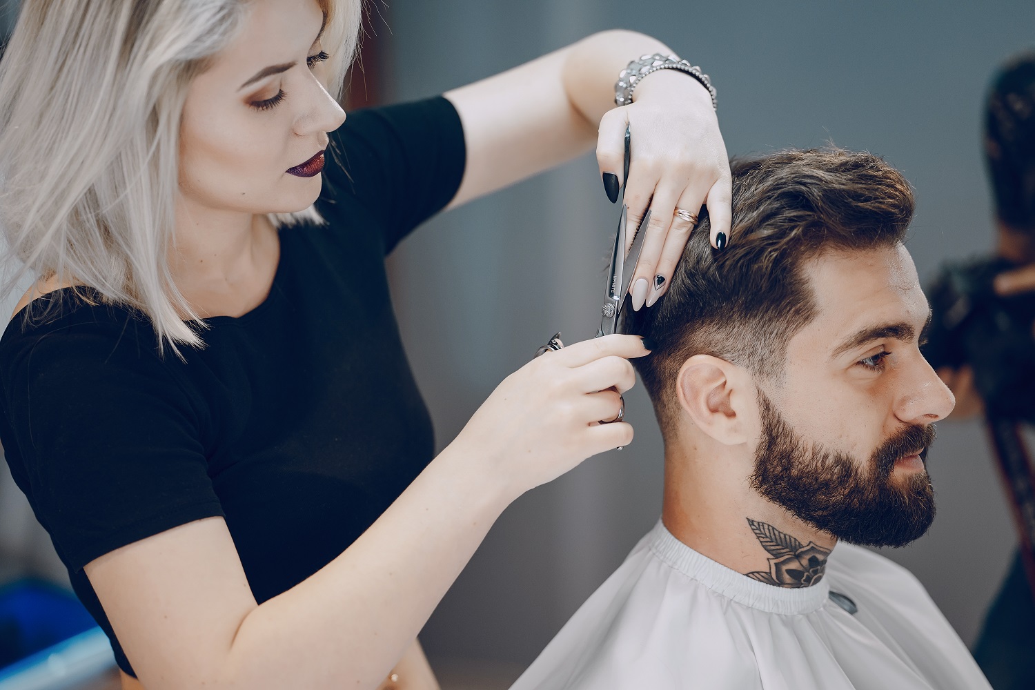 guy in the barbercos handsome young bearded guy sitting in an armchair in a beauty salon and the girl near him cuts his hair